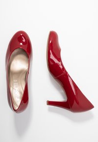 Tacchi alti in pelle verniciata rossa con punta arrotondata, design elegante, tacco di 10 cm e finitura liscia e lucida. L'interno presenta una fodera dorata.