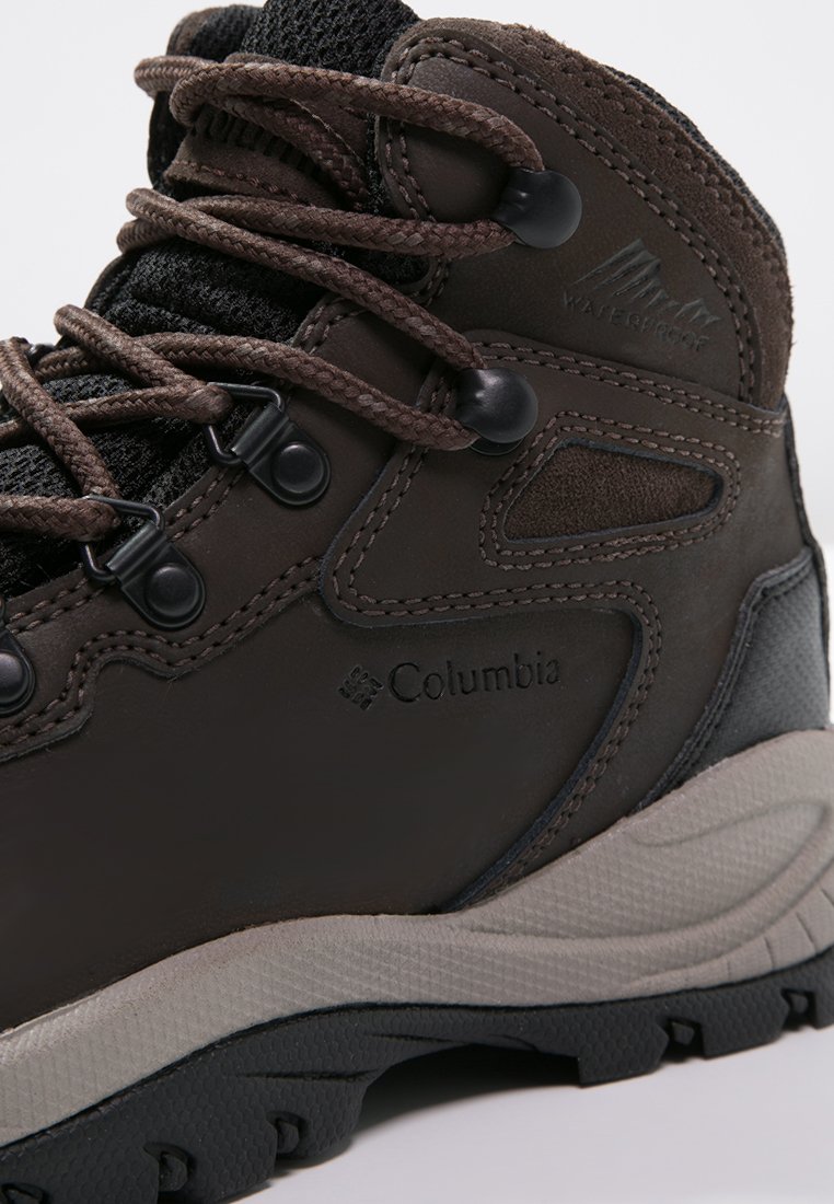 Stivale da trekking impermeabile marrone con parte superiore texturizzata, suola in gomma grigia e lacci marroni. Presenta il logo e occhielli rinforzati per una maggiore durata.