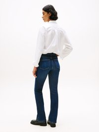 Weißes Langarmhemd mit Kragen, kombiniert mit dunkelblauen, weit geschnittenen Jeans. Die Jeans haben hinten Taschen und eine figurbetonte Passform.