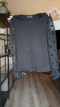 Must mustre top, mille varrukatega, millel on ühtlane keha ja läbipaistvad puffvarrukad, millel on mustad täpid. Materjal tundub pehme ja kerge.