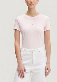 Světlounce růžové tričko s krátkým rukávem a kulatým výstřihem, s jemným logem na hrudi, spojené s bílými džíny s vysokým pasem.