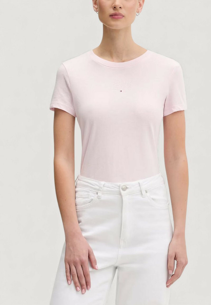 Světlounce růžové tričko s krátkým rukávem a kulatým výstřihem, s jemným logem na hrudi, spojené s bílými džíny s vysokým pasem.