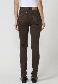 Jeans marrones ajustados con cintura alta, que presentan costuras decorativas en los bolsillos traseros y una etiqueta de cuero en la cinturilla.