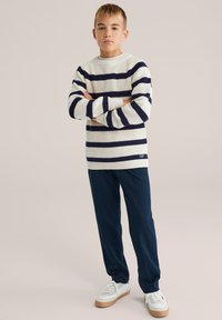 Prugasti pleteni pulover u krem boji i mornarskoj plavoj, s okruglim izrezom i rebrastim manžetama, uparen s mornarskoplavim hlačama i bijelim tenisicama.