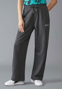 Szare dresy z luźnym krojem, z talią na sznurek, bocznymi kieszeniami i małym białym logo. Materiał wydaje się miękki i gładki.