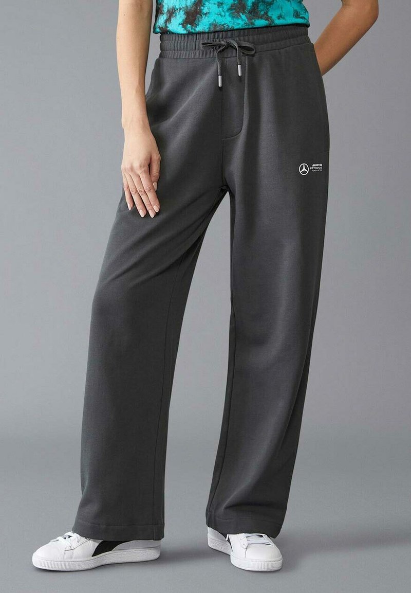 Szare dresy z luźnym krojem, z talią na sznurek, bocznymi kieszeniami i małym białym logo. Materiał wydaje się miękki i gładki.