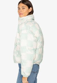 Lichtgewicht, mintgroene pufferjack met een wit golvenpatroon, hoge kraag, ritssluiting en zijzakken. Zachte textuur, oversized pasvorm.