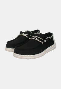 Scarpe di tela nere con suole e lacci bianchi in gomma. Il design presenta una punta arrotondata e un'accento a righe sul collo.