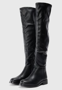 Botas negras por encima de la rodilla hechas de material sintético suave, con puntera redonda, tacón bajo y un zipper lateral para facilitar su uso.