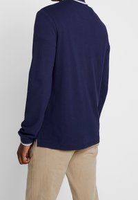 Marinblå långärmad t-shirt med rund hals, tillverkad av strukturerad bomull, med sidoklyftor och kontrasterande randiga detaljer vid kragen.