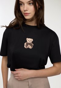 Czarny t-shirt z krótkim rękawem z grafiką pluszowego misia w leopardzim szaliku, wykonany z miękkiej bawełny. Prosty okrągły dekolt.