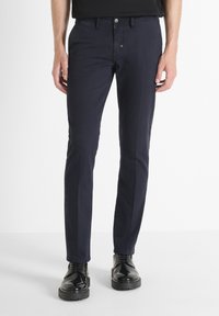 Pantalone u mornarsko plavoj boji od pamučne mješavine. Slim fit dizajn sa glatkom teksturom, pet džepova i kopčanjem na dugme. Upareni sa crnim cipelama.