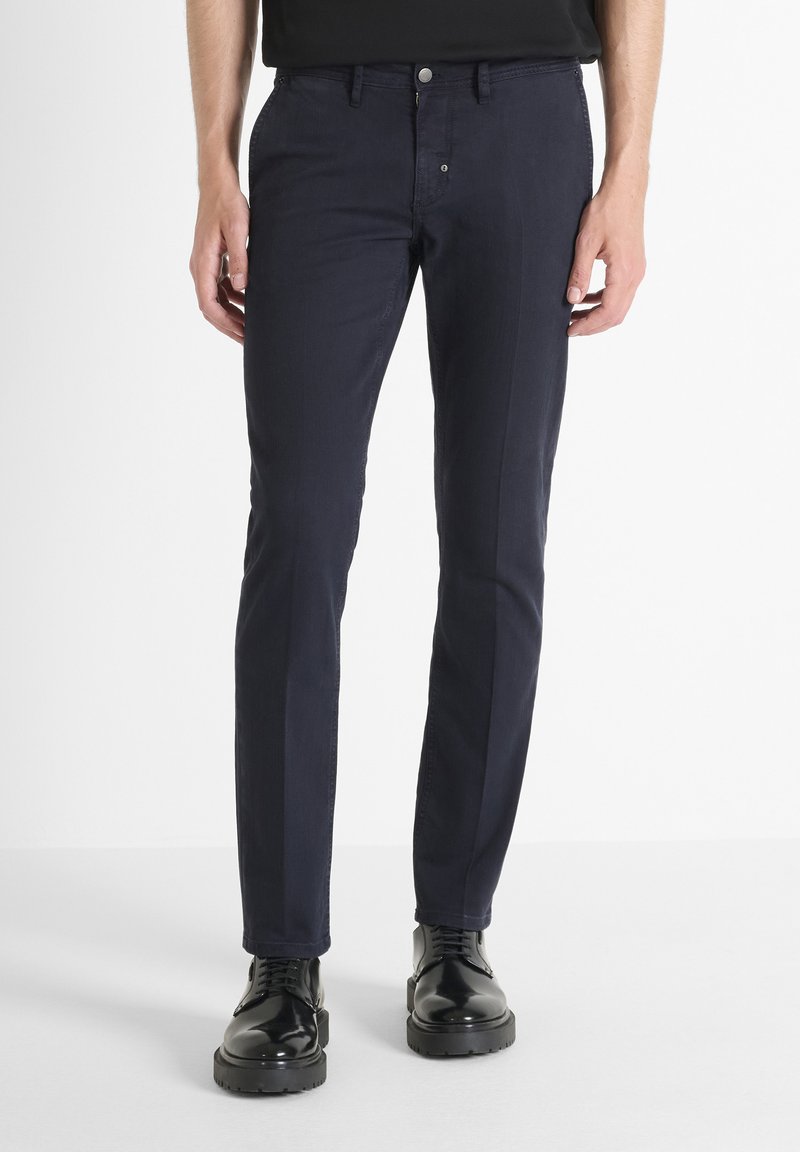 Pantalone u mornarsko plavoj boji od pamučne mješavine. Slim fit dizajn sa glatkom teksturom, pet džepova i kopčanjem na dugme. Upareni sa crnim cipelama.