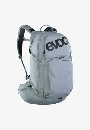 Mochila gris con tela duradera, compartimento principal grande, correas ajustables, bolsillo frontal y logo negro prominente.