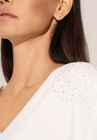 White soft fabric top with a V-neckline, featuring scattered crystal accents on the shoulder. Smooth texture and simple design.