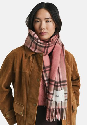 Écharpe à carreaux rose et gris en tissu doux, avec des bords à franges et une étiquette du logo GANT. Portée avec une veste en suède marron.