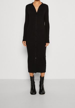Robe midi noire en tricot avec un col, des manches longues et des boutons sur le devant. Portée avec des bottines noires.