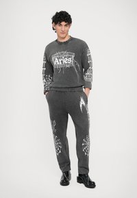 Sweatshirt cinzento e calças combinando com estampas gráficas brancas, apresentando teias de aranha e texto. Ajuste casual com punhos e cintura canelados.