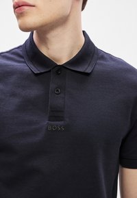 Μπλέ κοντομάνικο πόλο μπλουζάκι από υφή με τριπλή κουμπότρυπα και κεντητό λογότυπο "BOSS" στο στήθος. Απλός σχεδιασμός.