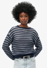 Suéter de punto azul marino y blanco con un patrón de rayas horizontales, cuello redondo y detalle de dobladillo acanalado, combinado con jeans de mezclilla claros.