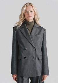 Szary dwurzędowy marynarka z dwoma guzikami, klapami z wyci�ęciem oraz kieszenią na piersi. Noszony na ciemnozielonym golfie. Gładka tekstura tkaniny.