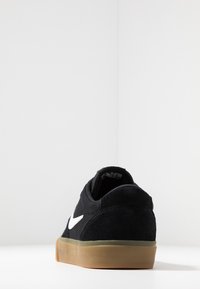 Svart mockaskor med vit swoosh-logotyp, lågprofil design, rund tå och sula av gummisulor. Strukturerad ovandel och vadderad krage.