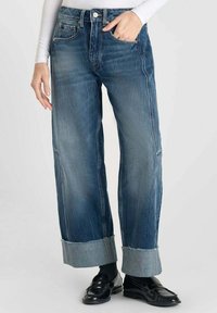 Jeans in denim a gamba larga con un lavaggio blu medio, caratterizzati da una vita alta, orli arrotolati e una leggera abrasione sulla parte anteriore.