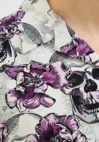 Cămașă cu mânecă scurtă, dintr-un material alb, cu imprimeu negru și violet de cranii și flori, incluzând flori detaliate și accente geometrice.
