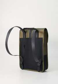 Sac à dos en tissu vert olive et noir, doté de deux poignées supérieures, de bretelles ajustables et d'une poche zippée sur le côté.