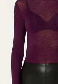 Durchsichtiger Langarm-Top in tiefem Burgunderrot, mit figurbetontem Schnitt und strukturierter Oberfläche. Kombiniert mit einem eleganten schwarzen Taillenbund.