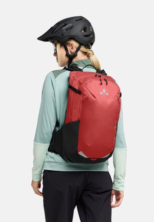 Zaino rosso e nero con un design elegante, tracolle regolabili e dettagli riflettenti, indossato da una persona con una maglietta a maniche lunghe verde menta.