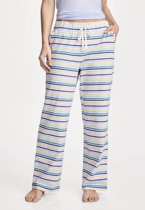 Person wearing loose, striped pajama pants with blue, yellow, and green lines, standing barefoot with one hand in a pocket.