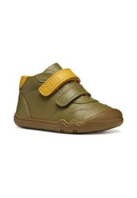 Scarpe in pelle verde oliva con una fascia in velcro gialla. Punta arrotondata, suola in gomma e dettaglio di cucitura visibile. Design compatto, alto alla caviglia.