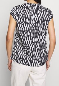 Svart- och vitrandig kortärmad topp med ett droppmönster, rund halsringning och lös passform. Tyget verkar slätt med en lätt lyster.