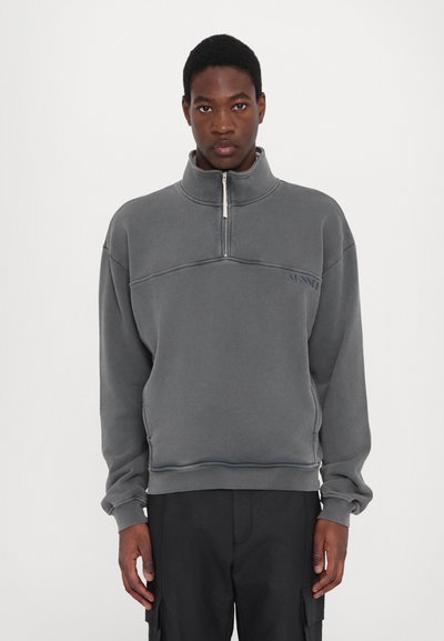 Sudadera gris de forro polar con media cremallera, cuello alzado, puños elásticos y un pequeño logo en el lado izquierdo del pecho. Material texturizado y suave.