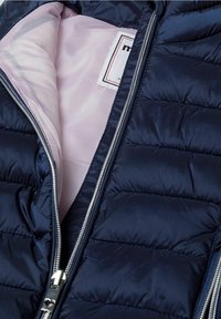 Marineblaue Steppjacke mit einem Innenfutter aus gestepptem Material und einem hellrosa Futter. Silberner Reißverschluss und Etikett befinden sich innen.