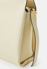 Krämfärgad läderväska med en strukturerad yta, har ett guldfärgat blixtlås och detaljer, samt en kontrasterande svart kant längs sömmarna.