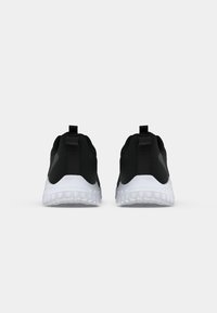 Paire de chaussures de sport noires avec semelles blanches vues de dos, avec des languettes au talon et un motif texturé de la semelle.