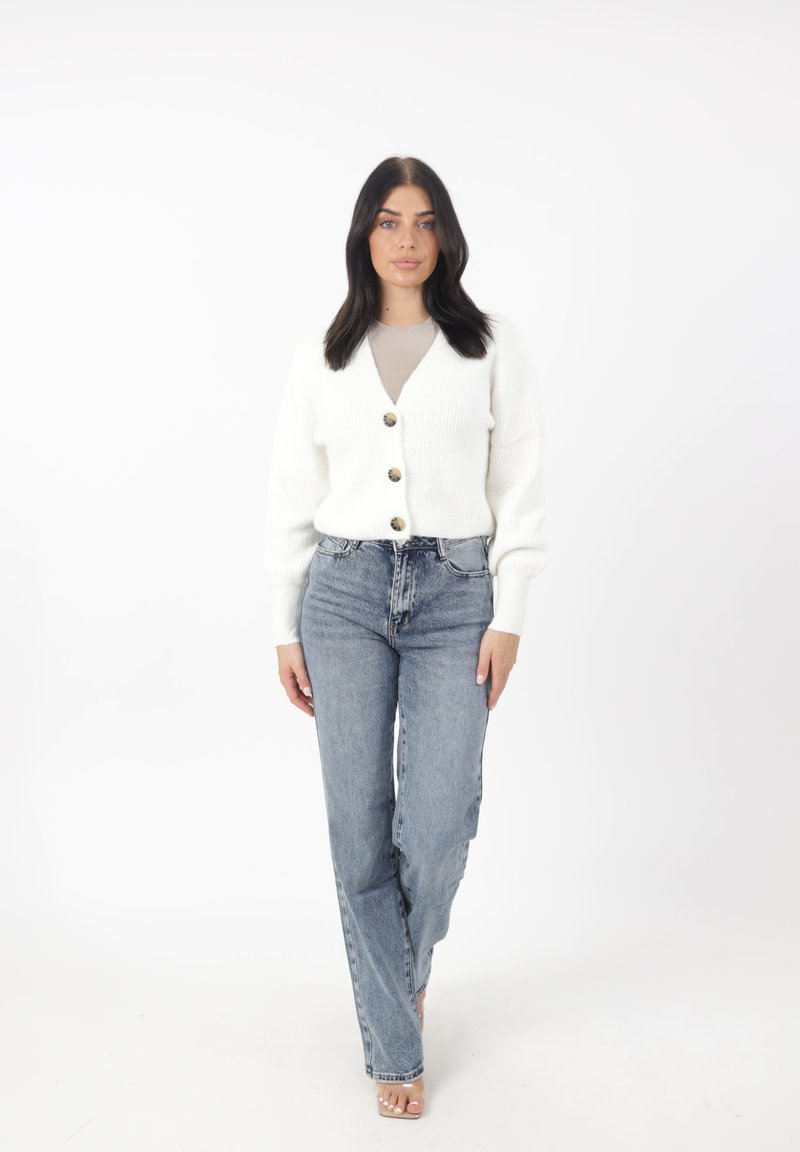 Cárdigan blanco acanalado con cierre de botones, combinado con jeans de tiro alto azul claro. Diseño sencillo, textura suave y ajuste casual.