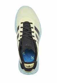 Žlté semišové tenisky s čiernymi pruhmi a šnúrkami, modrá vzorovaná vnútorná stielka a textúrovaná mäta zelená podrážka. Navrhnuté pre pohodlie a štýl.