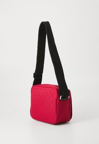 Borsa a tracolla rossa in tessuto con un motivo check testurizzato, cintura regolabile nera, forma rettangolare e chiusura con zip. Accenti in metallo argentato.