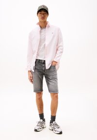 Lys rosa skjorte med knapper over en hvit og grå stripete T-skjorte, kombinert med grå denimshorts og sølvfargede sneakers. Mørk caps og grå sokker.