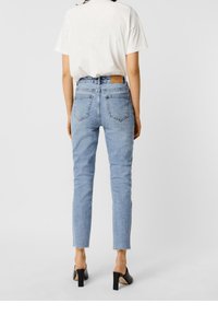 Světle modré džíny s vysokým pasem, slim fit, se světlejší texturou a roztrhaným lemem. Kombinované s bílou košilí a černými podpatkovými muly.