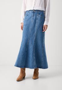 Denim rok in medium blauw, A-lijn ontwerp met twee zijzakken, onafgewerkte zoom en gecombineerd met bruine haklaarzen.