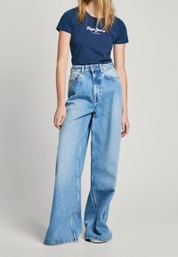 Granatowy t-shirt z krótkim rękawem z białym logo, zestawiony z jasnoniebieskimi, szerokimi dżinsami z wysokim stanem, wykończonymi efektem sprania i dużymi przednimi kieszeniami.