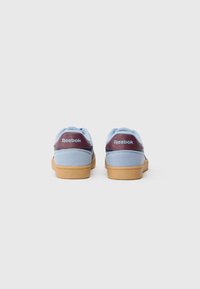 Niebieskie zamszowe sneakersy z bordowym akcentem na pięcie i beżową gumową podeszwą. Logo Reebok widoczne na tyle.