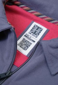 Marineblauwe zip-up jas met een rode binnenkant, voorzien van een patroon op de kraag, een stoffen label met QR-code en contrasterende stiksels.