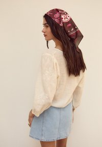 Svetlo bež srajca iz lana z napihnjenimi rokavi in vezenimi detajli, v kombinaciji z svetlo modrim denim mini krilom in patterned rjavim šalom.