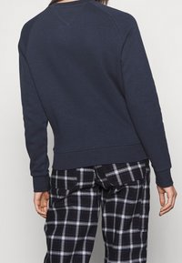 Sweatshirt bleu marine avec des manches raglan, des poignets et un ourlet côtelés, fabriqué en tissu doux. Associé à un pantalon à motifs carreaux noir et blanc.