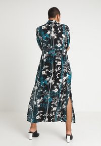 Lång, svart blommig klänning med blå och vita mönster. Har en hög slits, långa ärmar och en åtsittande midja för struktur.